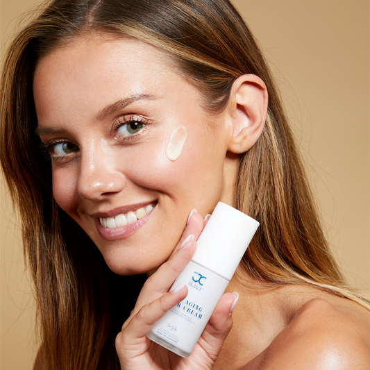 Frau mit aufgetragener Anti-Aging Super Cream auf der Wange, Pumpspender in der Hand