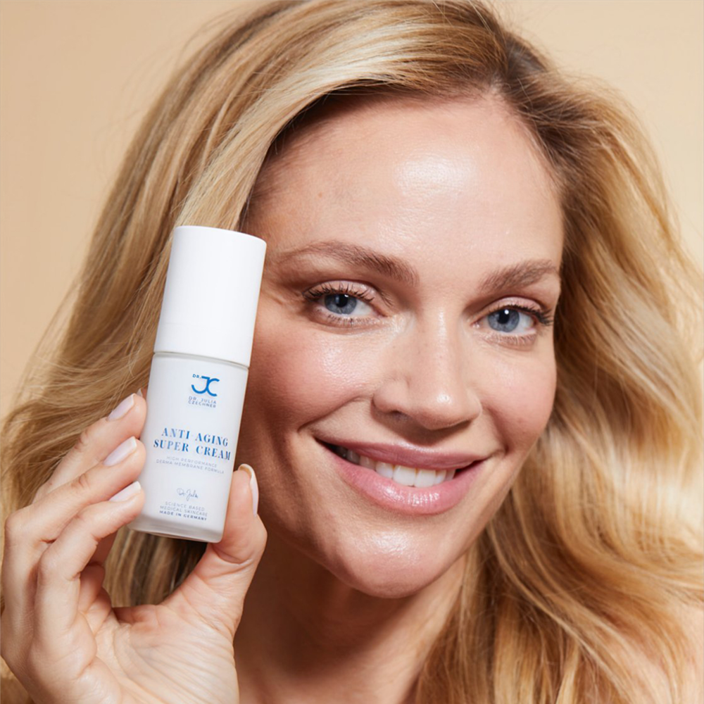 Frau hält den Pumpspender der Anti-Aging Super Cream neben ihr Gesicht